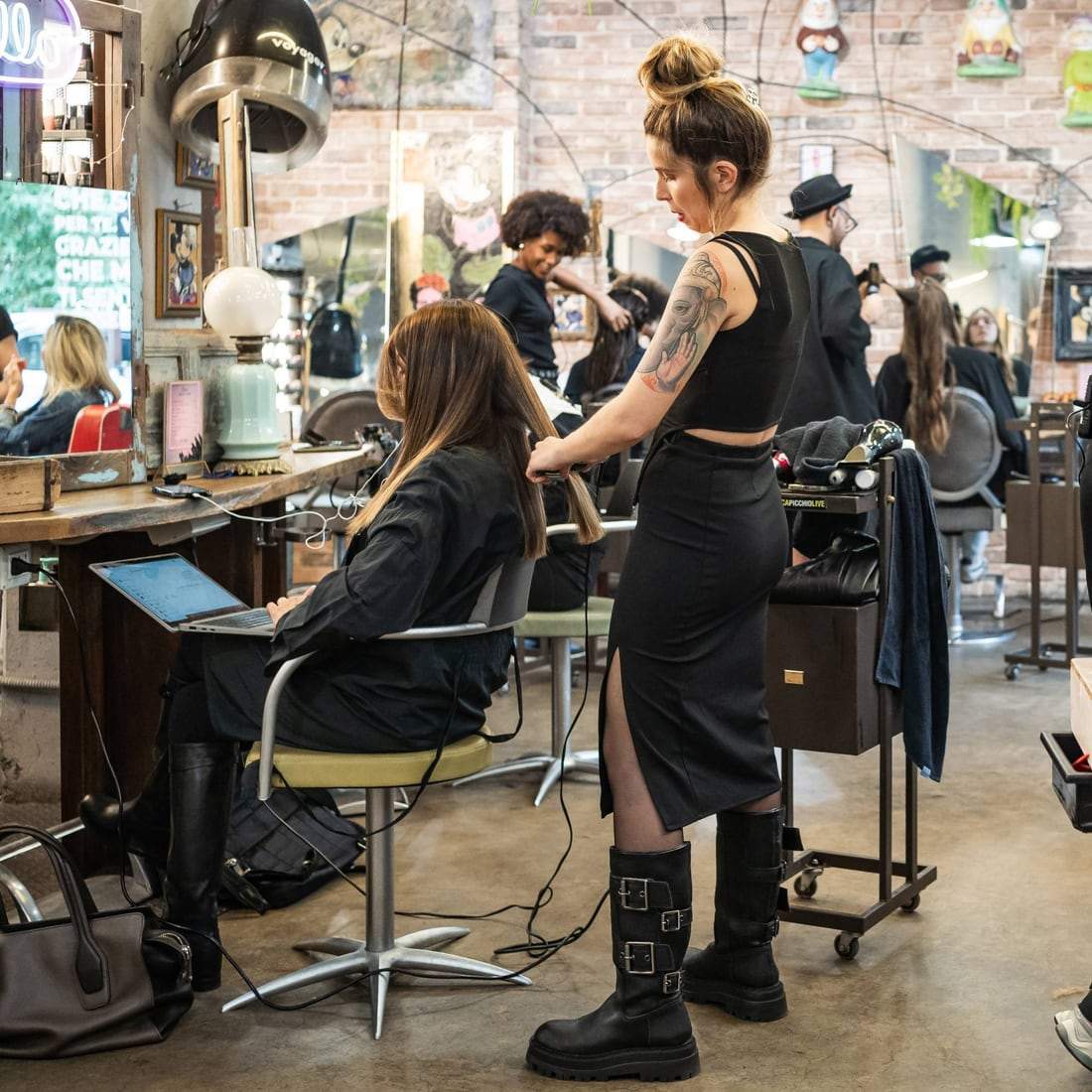 Un salone pieno: una parrucchiera piastra i capelli a una cliente, dietro altri al lavoro