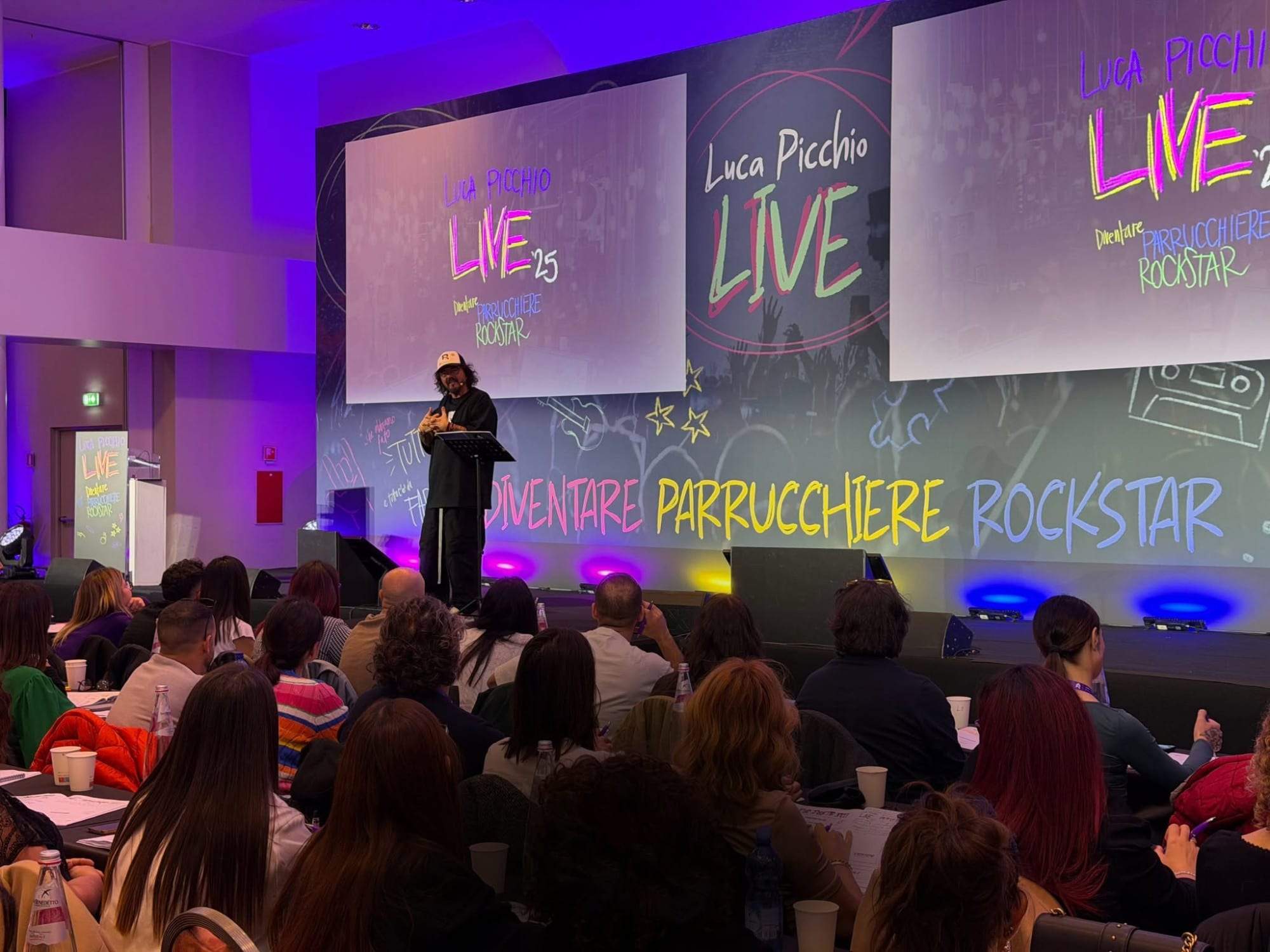 Luca Picchio sul palco del Live '25 davanti alla platea, sotto la scritta Diventare Parrucchiere Rockstar