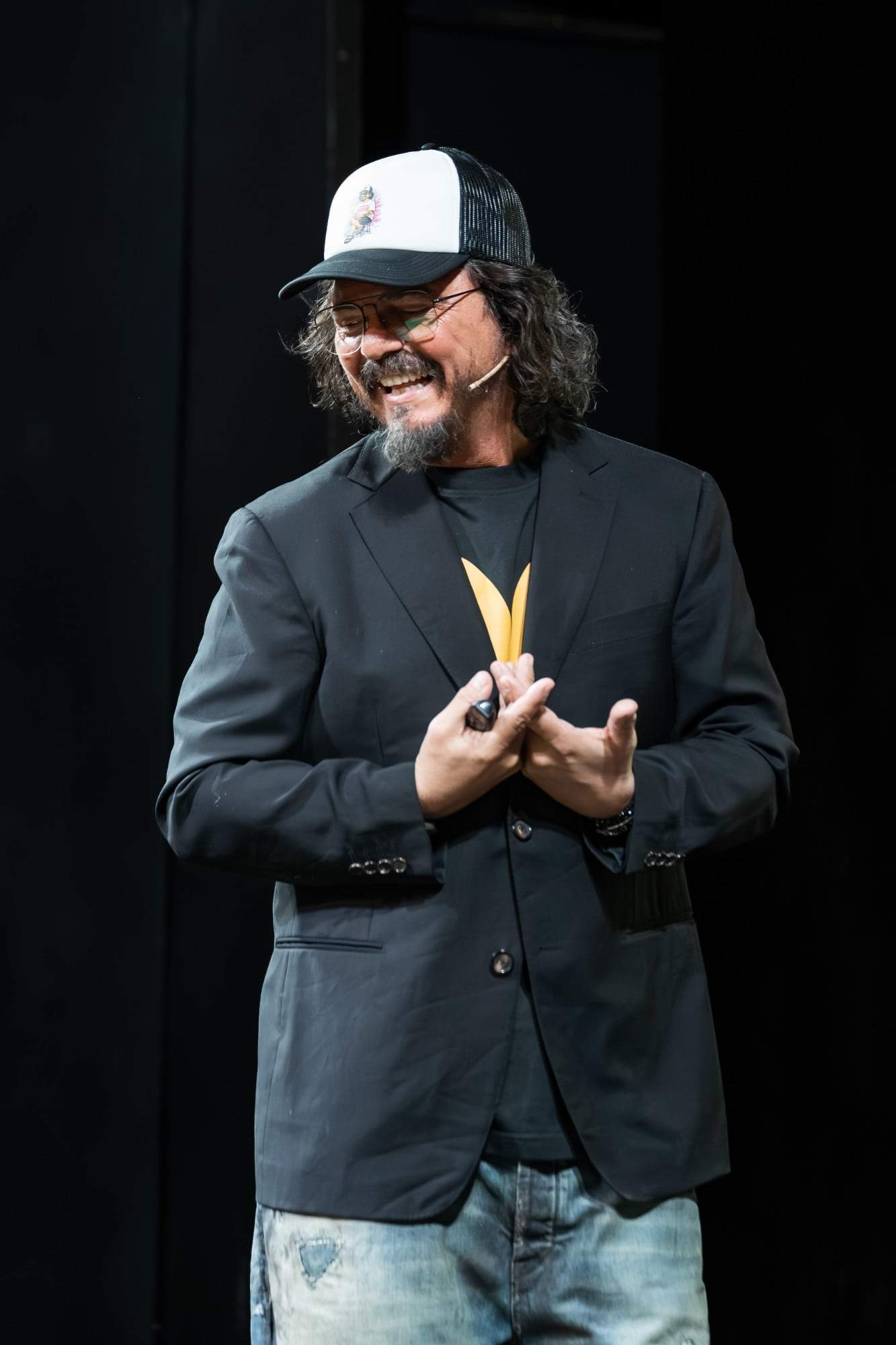 Luca Picchio sorridente sul palco, con il cappellino e la giacca nera
